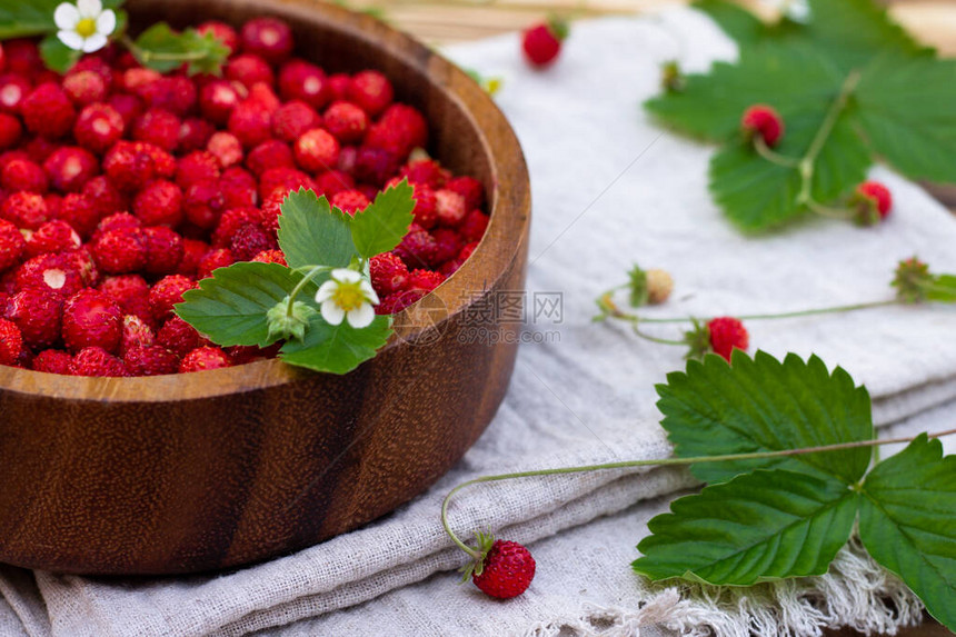 一碗红色的成熟野草莓和花朵在旧木质表图片