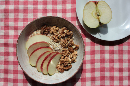 红白餐巾上的古董碗里有健康的胡桃红苹果燕麦图片