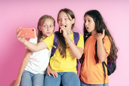 三个十几岁的女孩笑着用粉红色的背景图片