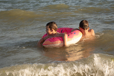 一个5岁的男孩带着他10岁的哥带着一个甜圈形状的充气圈在海里游泳两兄图片