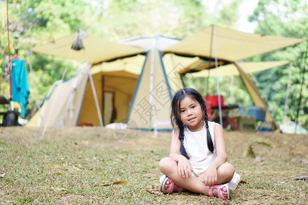 亚洲儿童可爱或小女孩露营者坐在草地坪和自然露营帐篷或小屋营地背景图片