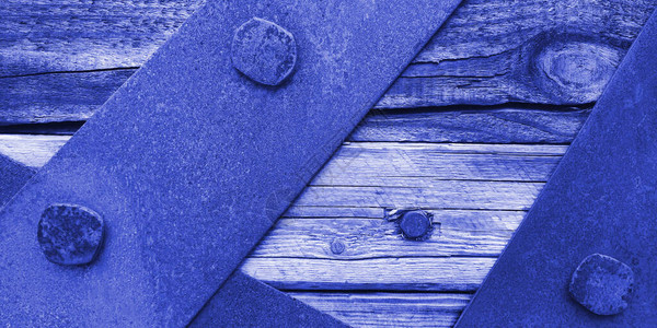 锈迹斑的铁皮或板条的特写纹理用蓝色和紫色调用螺栓固定在老化的木板上图片