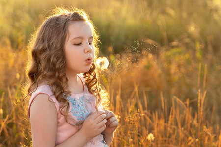 可爱的小女孩长发卷在日落光下吹花朵自然概念过敏童年复制空图片