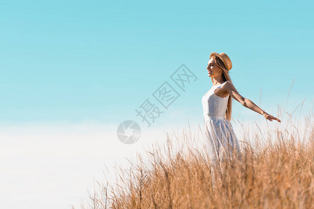 穿着草帽和白礼服的金发女人站在山图片