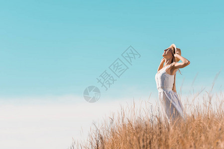 身着白裙子的年轻女子在蓝天对立的草丘上站图片