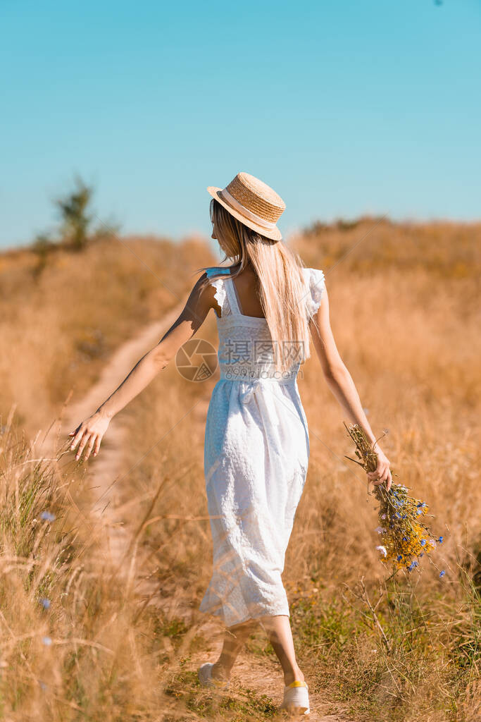 身着白裙子和草帽的年轻女子在草地上行走时图片
