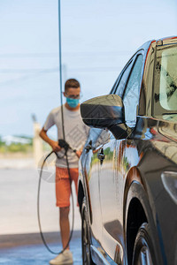 一个拿着高压喷水棒的失焦年轻人正在清洗一辆汽车的特写洗图片