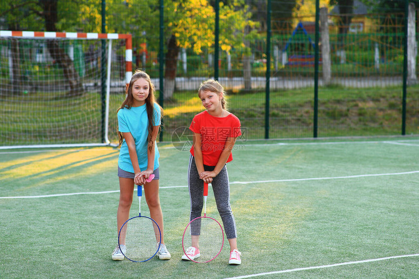 两个女孩在足球场上拿着羽毛球拍女学生放学后参加体育运动夏天在户外运动绿地上穿图片