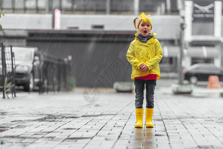 穿着黄色雨衣和橡胶靴的女孩在停车场的水坑里图片