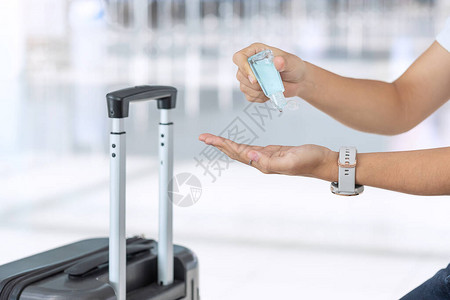 妇女在机场拿着手提行李袋后用酒精凝胶消毒剂清洁手图片