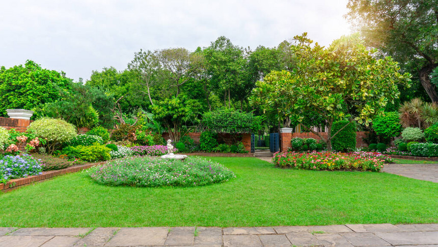 美丽的英式小屋花园光滑的绿草坪上色彩缤纷的开花植物和一群常青树图片