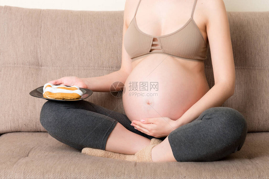 关闭年轻孕妇喜欢吃美味的蛋糕在家里的沙发上休息怀孕期间的不图片