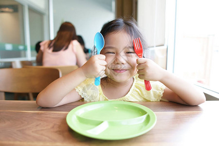 亚洲儿童可爱的饥饿或小女孩拿着五颜六色的勺子和叉子图片