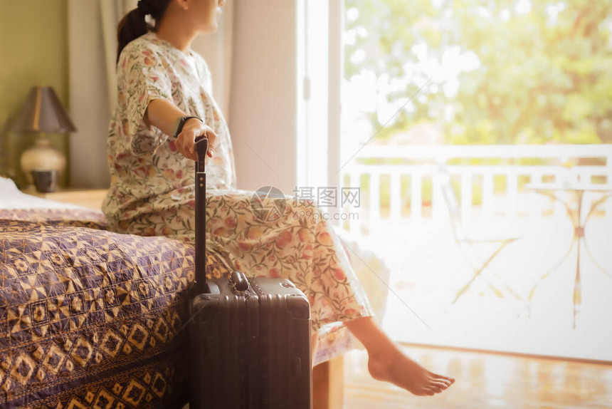携带行李的女旅行者坐在旅馆房间的床上图片