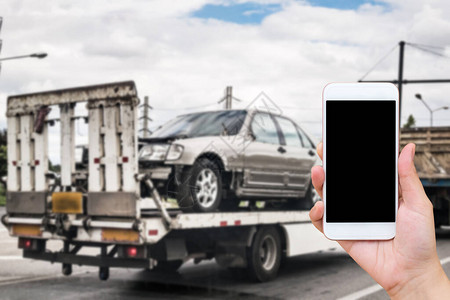 使用移动智能手机进行紧急路边应急交通服务的手与交通事故背景后拖车吊图片