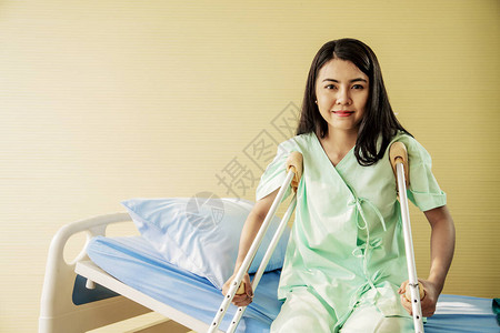 快乐的年轻女病人在病房里拄着拐杖坐在床上的画像医疗保健和图片