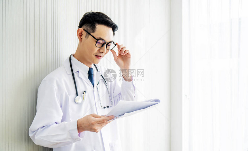 身着实验室大衣的年轻亚洲医生男子向下看他的病人笔记图片