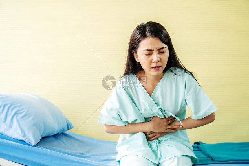 坐在医院床上腹部疼痛食物中毒时胃痛的女病人图片
