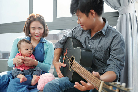越南年轻人弹吉他和唱歌给女儿听为图片