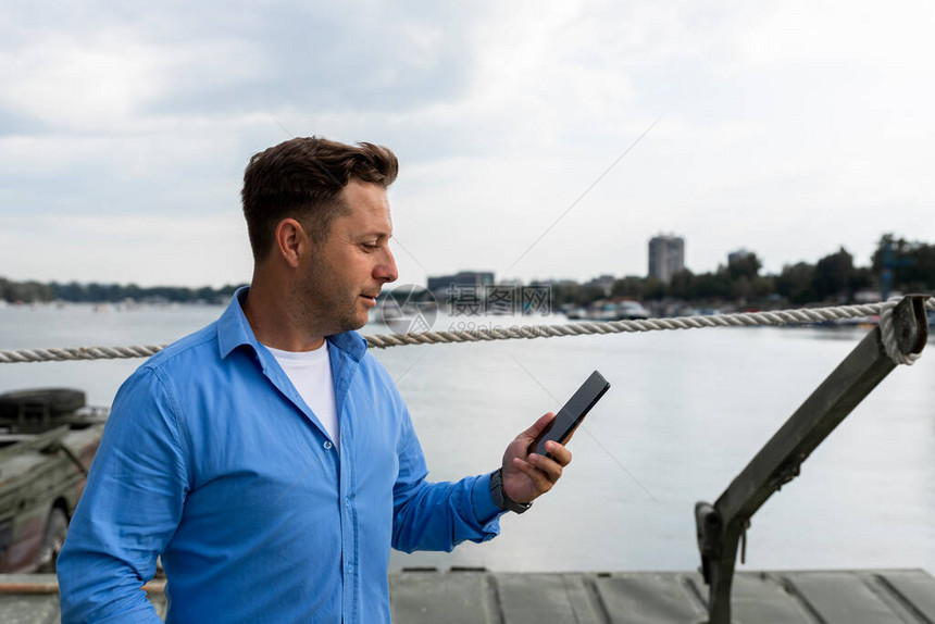 男人手里拿着智能手机在港口的河边航图片