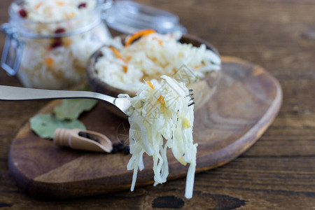 自制酸菜或桶白菜在质朴的木制背景上的叉子上背景是一碗卷心菜准备图片