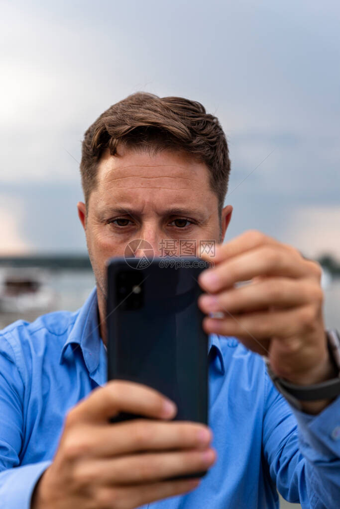 一个人在河边手里拿着智能手机并拍照图片