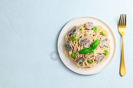 意大利面配奶油酱香菇和浅蓝色背景上的绿色罗勒图片