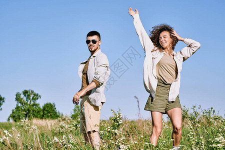 快乐的年轻女子在青草中跳舞与蓝天空对抗表达欢乐和喜悦而她的图片