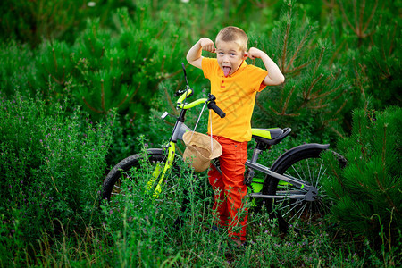 一个穿着橙色衣服的男孩夏天在绿色草地上玩弄着一辆自行车在青图片