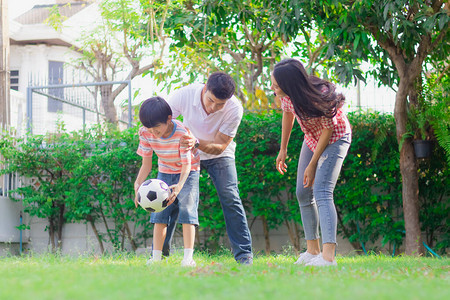 快乐的家庭父亲母亲和儿子在家里的院子里一起踢足球作为活动父母和孩子之间的关系或纽带享受周末的背景图片