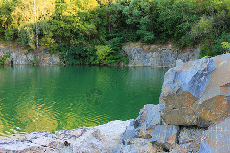 夏季的高山湖泊用氡水淹没旧花岗岩采石场的全景与石块绿树和干净图片