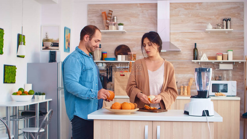女人在厨房里剥橙子做营养冰沙丈夫穿着牛仔衬衫快乐的家庭用新鲜水果一起制作有机健康新鲜营养美图片