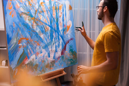 年轻的艺术家站在艺术工作室的绘画前画一幅杰作现代艺术作品在画布上绘画图片