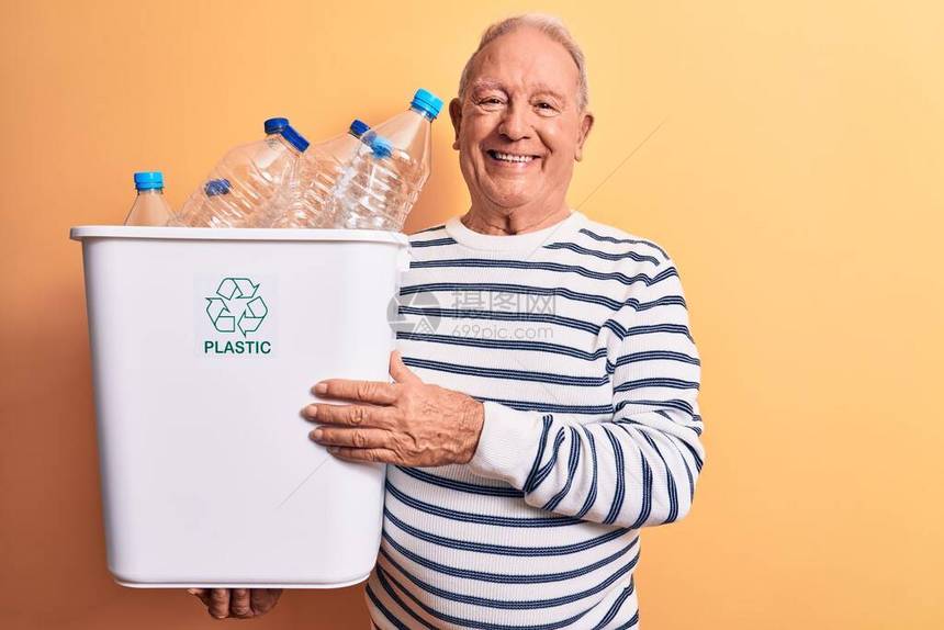 头发灰白的老帅哥回收拿着装满塑料瓶的废纸篓图片