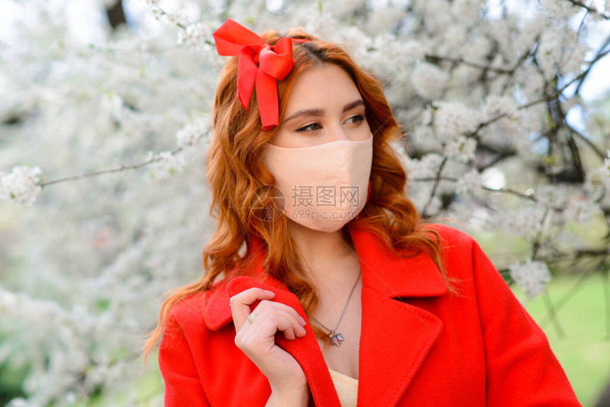 贴近红发女孩的肖像穿着红色大衣在一棵开花樱桃树下戴着图片
