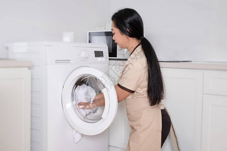 年轻的亚洲美女佣将洗衣机的白衣服背景图片