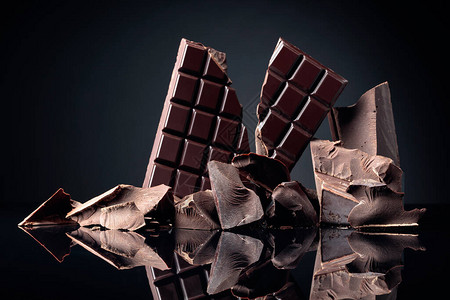 黑色反射背景的破碎巧克力棒和暗巧克力片复制空图片