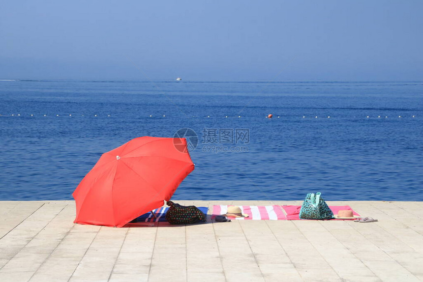 雨伞海滩毛巾帽子和带海滩用品的袋子在水边图片