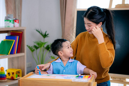 学前班教室里的亚洲老师教她的学生用彩色铅笔在有背景的桌子上画纸图片