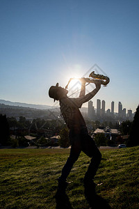 一位男子在太阳升起的山丘上玩高空萨克斯手的轮廓图片