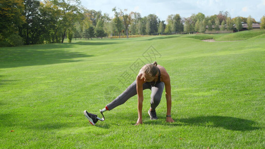 残疾妇女在公园里伸展双腿运动型女士准备在户外慢动作锻炼在绿色草地上锻图片