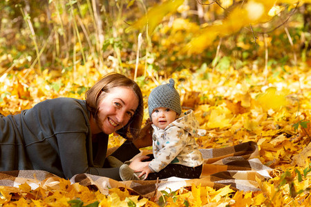 年轻母亲在阳光明媚的日子里秋天公园与婴儿共度时光图片