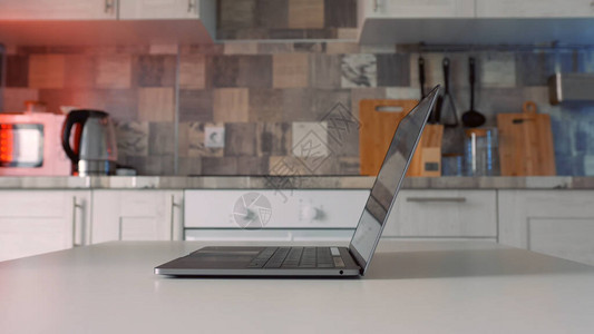隔离期间在家工作的概念打开站在厨房白桌上的新银色笔记本电脑的背景图片