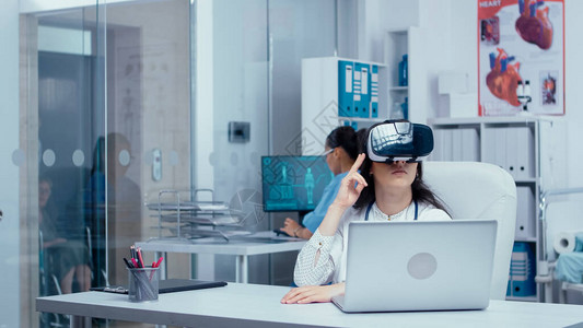 年轻的女医生在私人现代诊所使用虚拟现实耳机进行医学研究图片