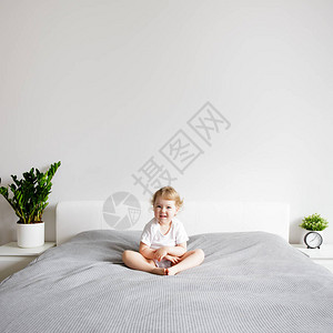 坐在现代卧室床上的快乐小女孩在白墙背图片