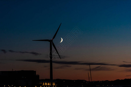 打蜡的新月在夜间从风力涡轮机后面经过图片