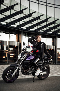 穿着黑色摩托车夹克的漂亮女孩坐在一辆黑色运动摩托图片
