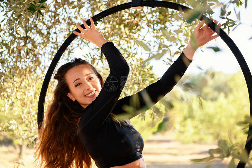 年幼的杂耍女孩在夏季在橄榄树间空中小圈或圆圈上微笑和摆姿图片