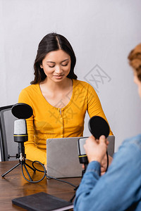 在采访演播室的人时使用笔记本电脑对年轻的年青亚洲无线电台主机进行选背景图片