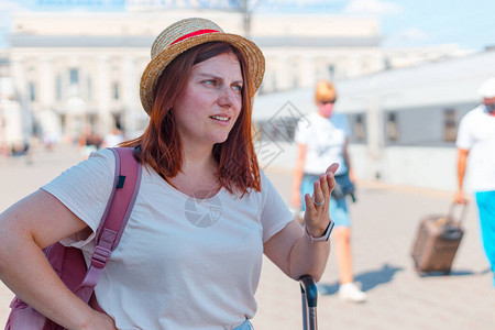 身戴帽子背着包和手提箱的年轻红发女游客图片